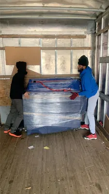 Two movers positioning a wrapped piano inside a moving truck